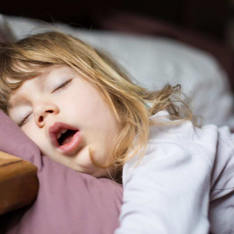 Pediatric Airway Issues: More Common Than You May Think, funny face expression with open mouth of blonde caucasian three years old child, sleeping on king bed