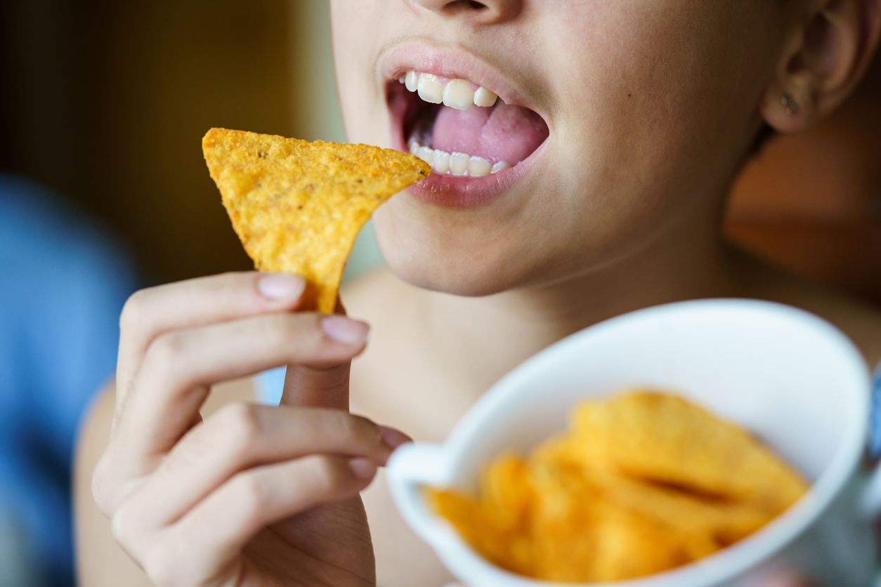 why kids get cavities, Unrecognizable girl about to eat spicy tortilla chip at home