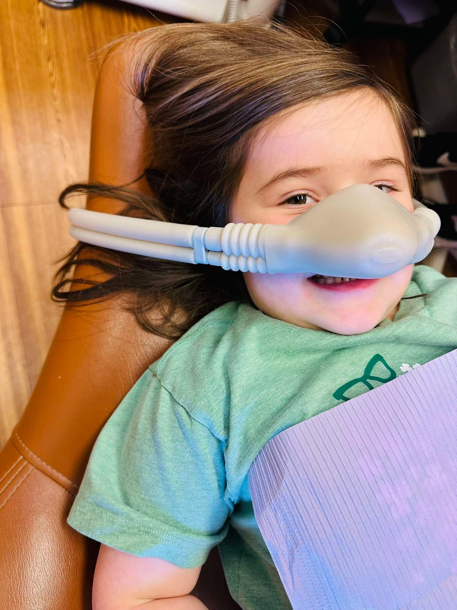Child relaxing in a dental chair while receiving nitrous oxide sedation at a pediatric dental appointment.