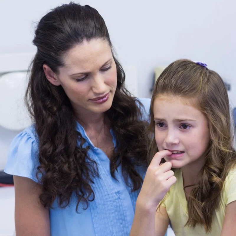 Concerned mother comforting her anxious young daughter who is biting her nails.