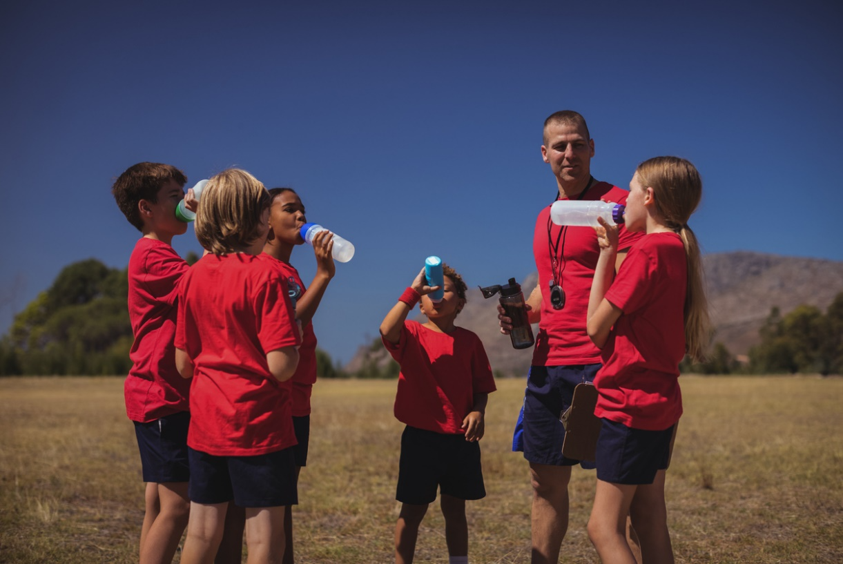 Children drinking water during outdoor summer sports activities to support hydration and healthy dental habits.