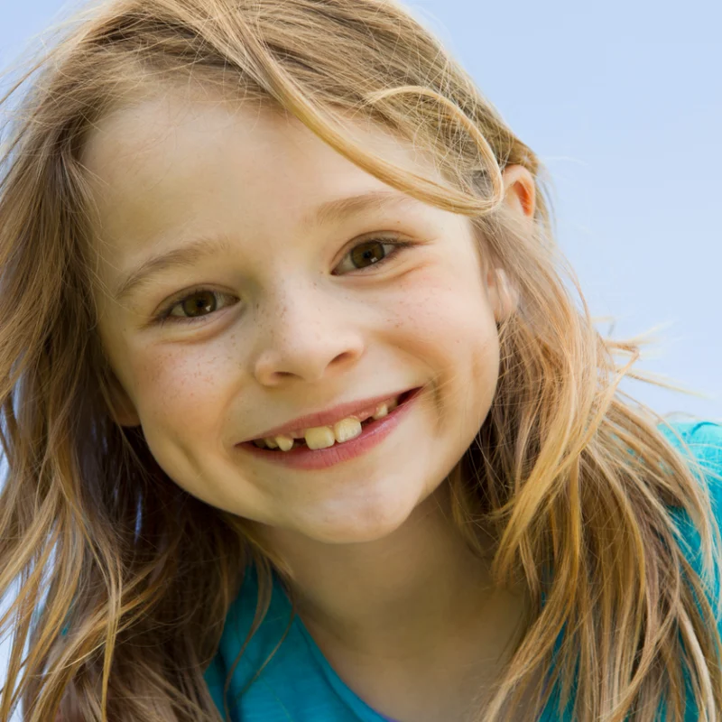 Young child smiling while holding a recently lost baby tooth, illustrating a common stage of childhood dental development.