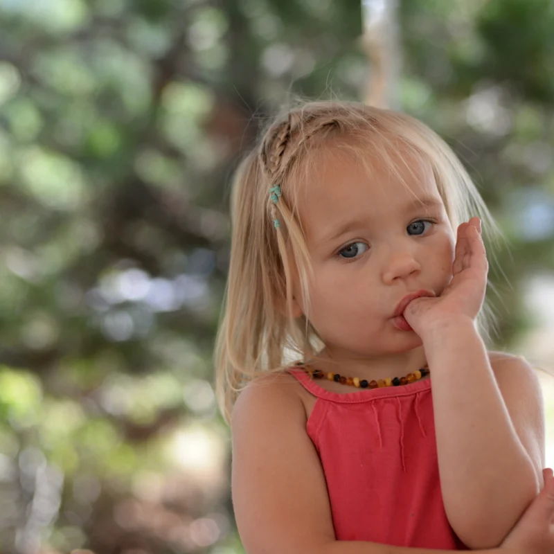 Close-up portrait of a young blonde girl with blue eyes and a braid, sucking her thumb.