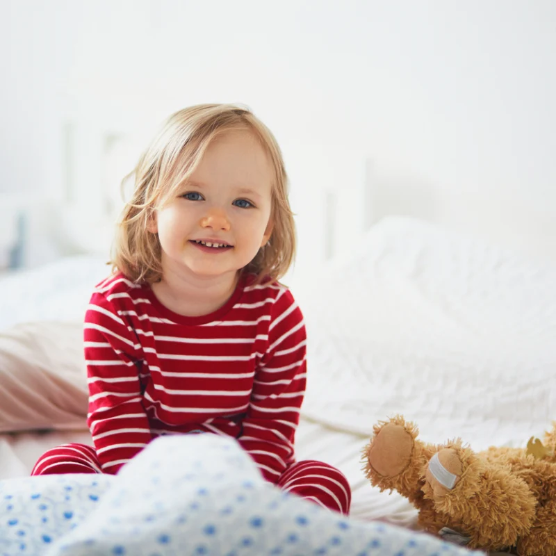 Young child in pajamas smiling while sitting on a bed.